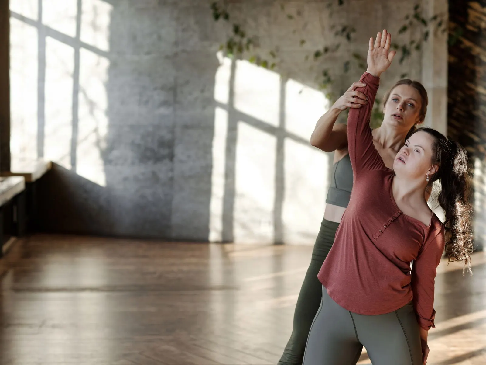 A woman with Down syndrome stretching during a yoga session, guided by an instructor