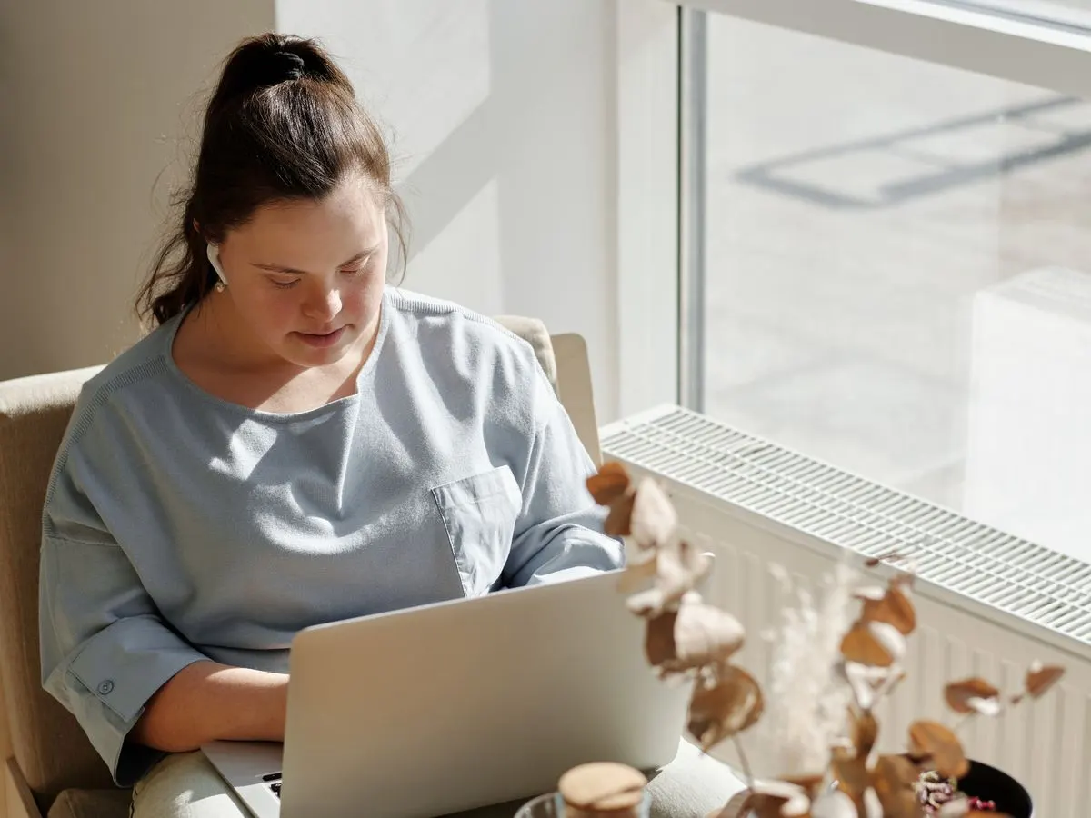 A woman with Down syndrome working at a laptop by a window