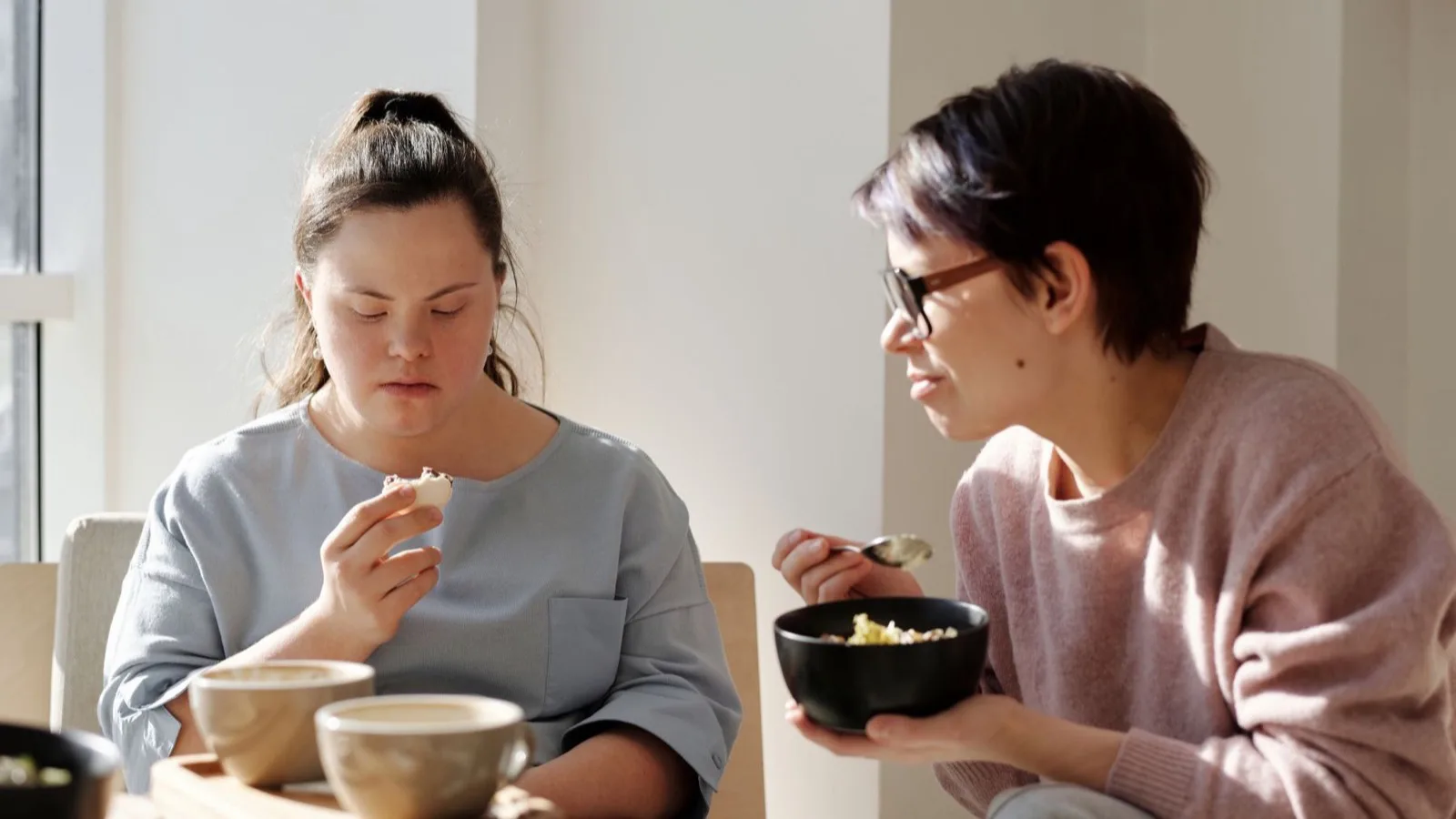 Two women sharing a meal at a table, one of them with Down syndrome